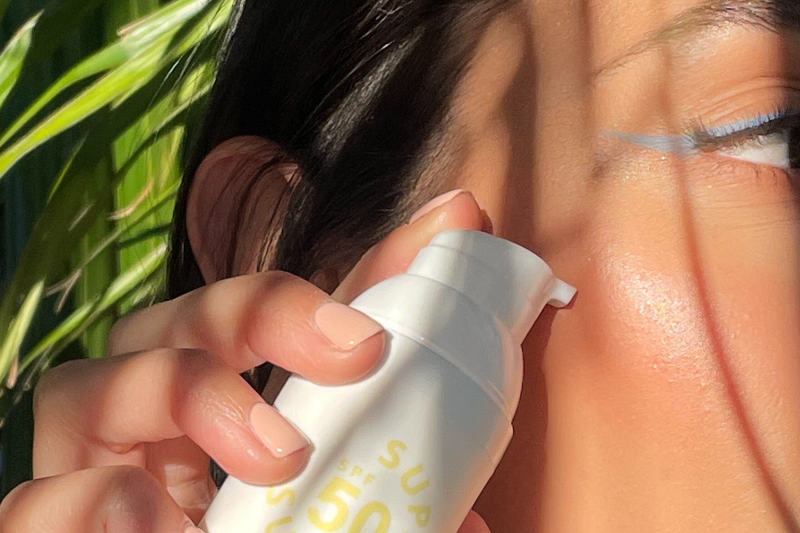 A woman holding a sunscreen SPF 50 bottle near her face.